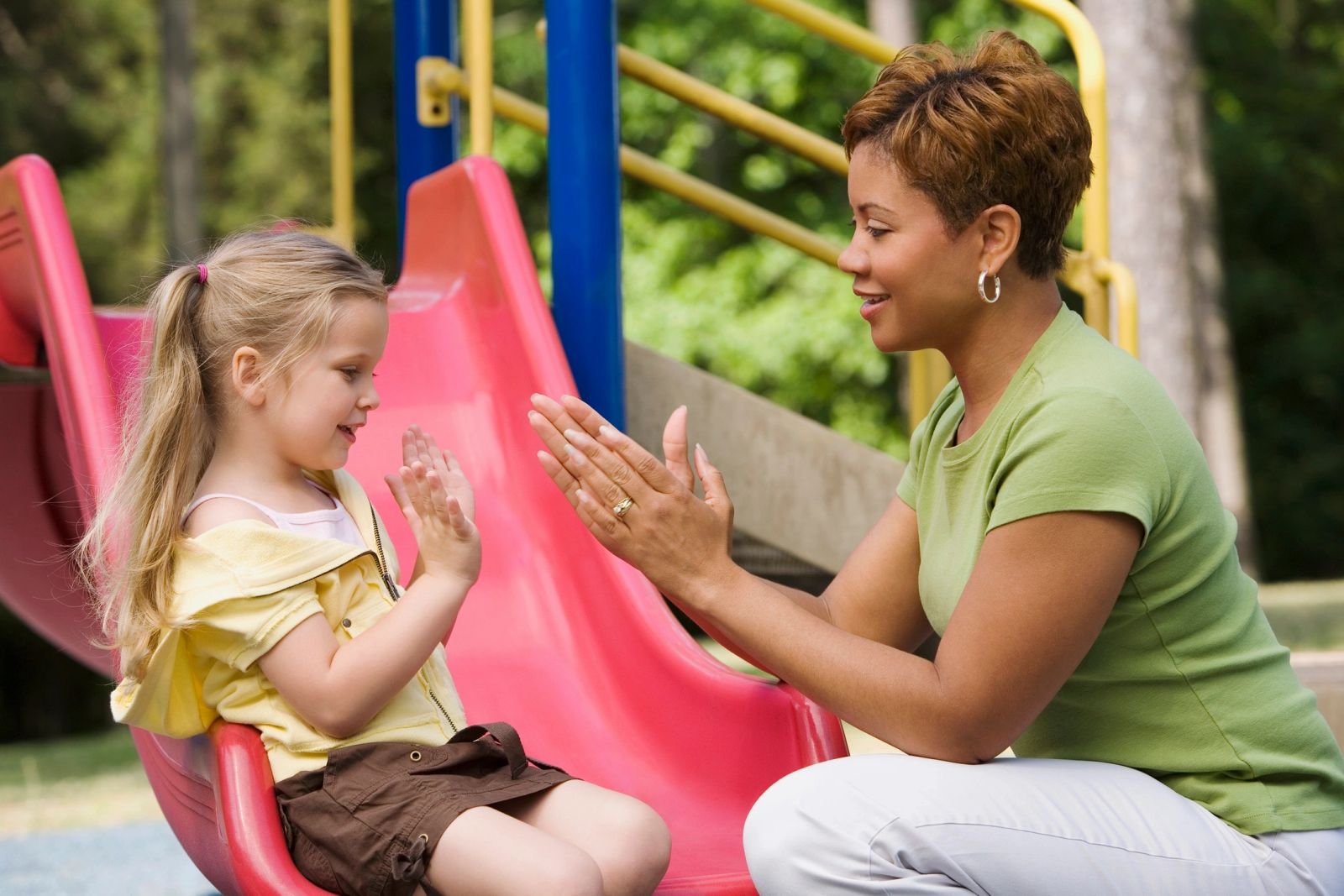 A nanny playing a clapping game with a little girl on the playground